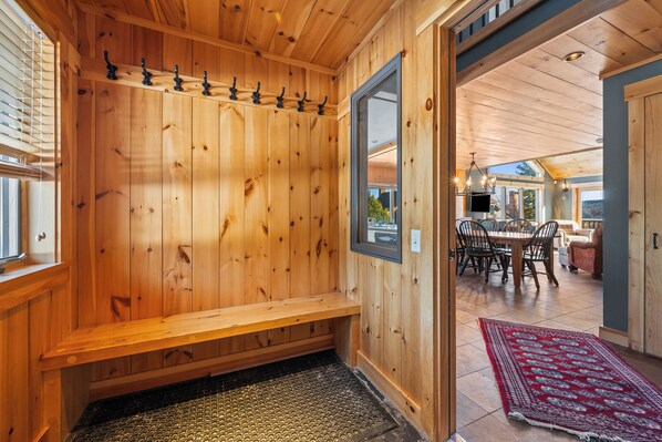 A wooden interior with a bench, a door leading to a dining area, and a patterned rug.