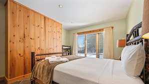 A bedroom with a wooden wardrobe, a bed with white linens, a window with blinds, and a lamp on the nightstand. - Rock Pond 36 | Ski-In/Ski-Out Saddleback Mountain Condo (Rangeley)