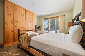 Een slaapkamer met een houten garderobe, een bed met witte lakens, een raam met zonwering en een lamp op het nachtkastje.