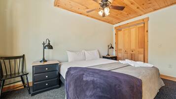 Une chambre à coucher comprenant un lit, deux tables de chevet avec des lampes, une chaise, une armoire en bois et un ventilateur de plafond.