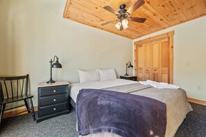 Een slaapkamer met een bed, twee nachtkastjes met lampen, een stoel, een houten garderobe en een plafondventilator.