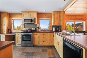 A modern kitchen with wooden cabinets, a stainless steel oven, a microwave, and a dishwasher. There are windows providing natural light and views of the outdoors.