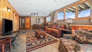 A spacious living room with a television, seating area, and large windows. - Rock Pond 36 | Ski-In/Ski-Out Saddleback Mountain Condo (Rangeley)