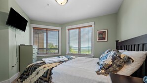 Un dormitorio con cama, televisor montado en la pared y dos ventanas con persianas.