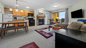 Una sala moderna con chimenea, un comedor con muebles de madera y una cocina con armarios y electrodomésticos de madera.