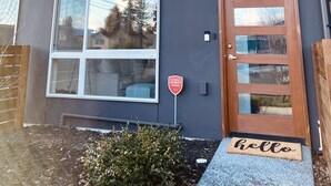 Moderni, kaksikerroksinen talo, jossa on suuret ikkunat, puuovi ja eteisessä tervetulomatolla varustettu oviaukko.