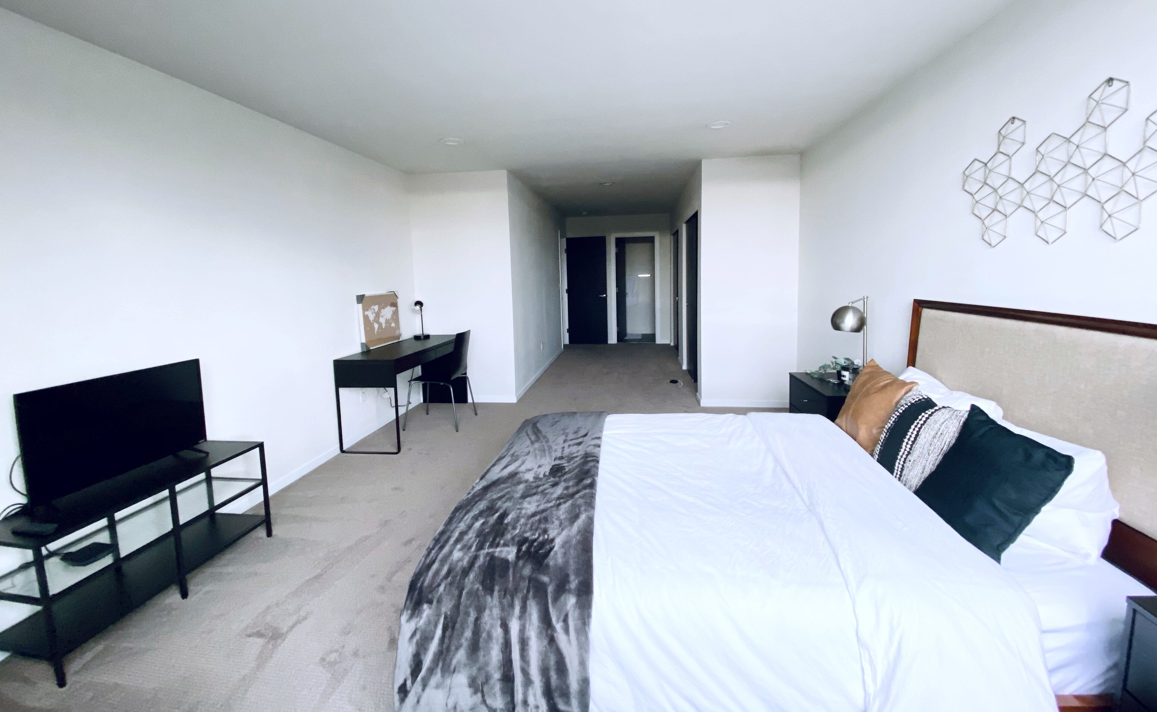 Een moderne hotelkamer met een groot bed, een bureau, een televisie en uitzicht op de gang.