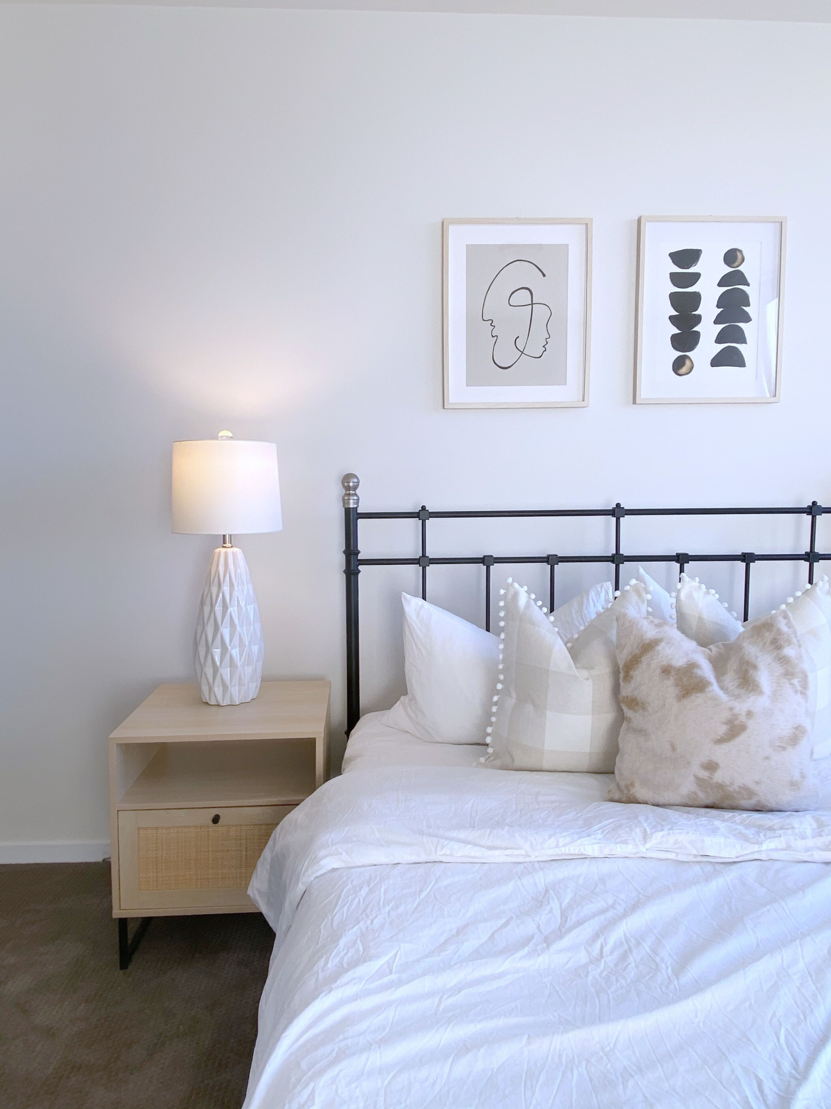 A neatly arranged bedroom with a bed, pillows, a bedside lamp, and two framed artworks on the wall.