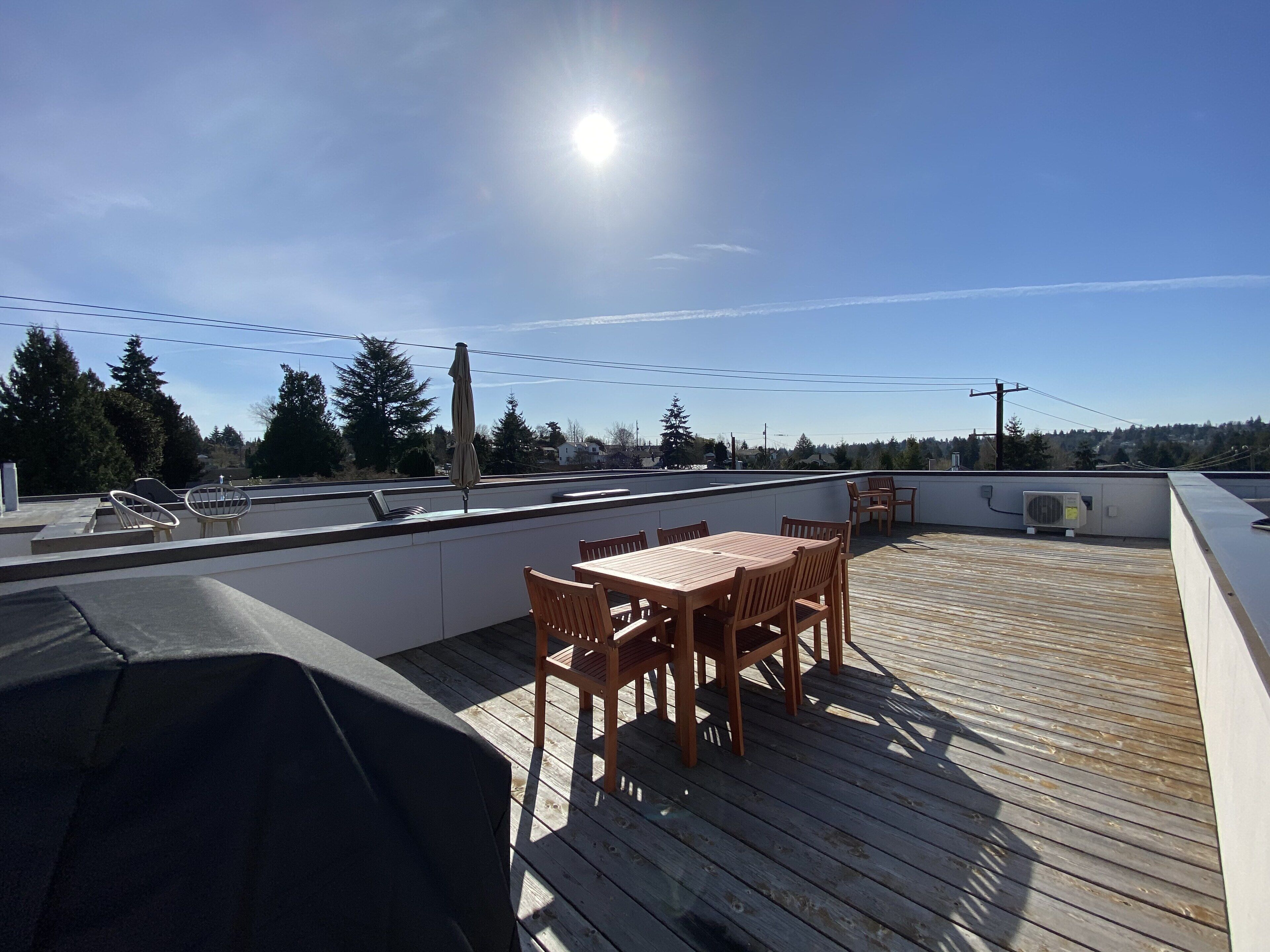 A rooftop patio with a wooden table and chairs, a grill, and a view of the surrounding area.