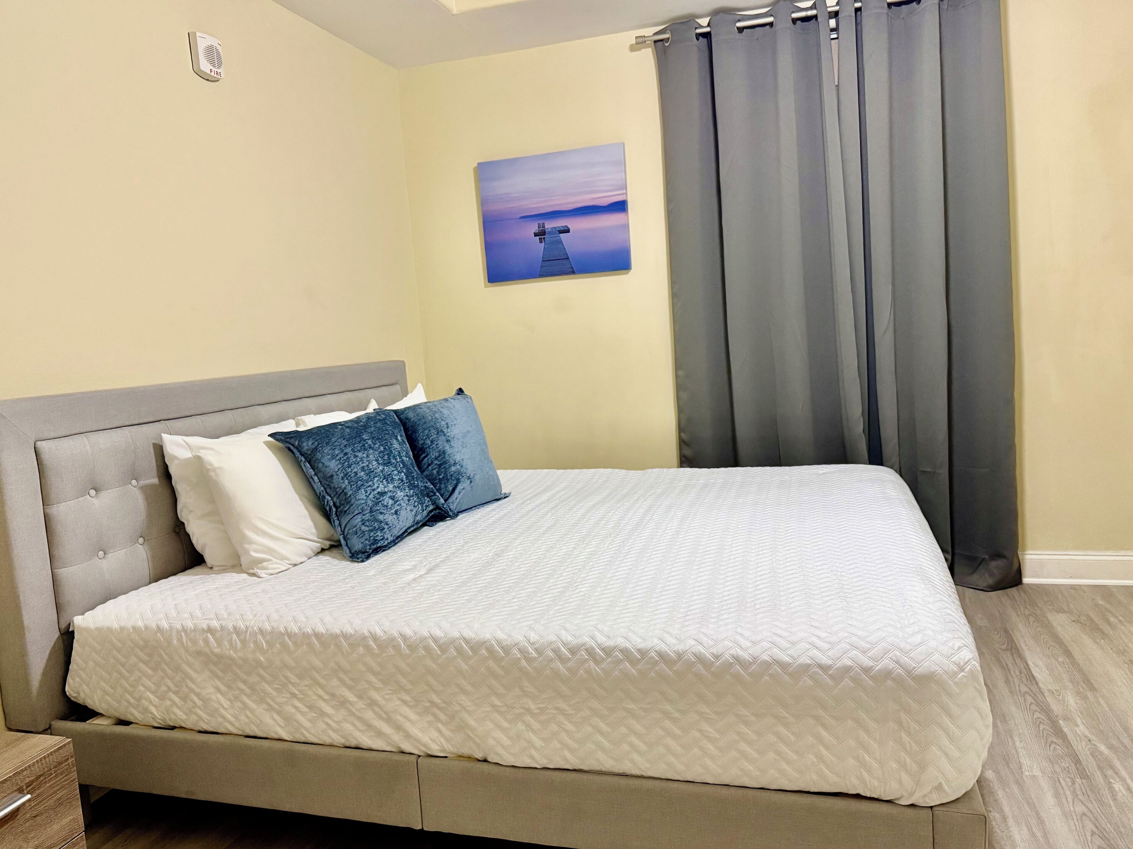 Un lit recouvert d’une couette blanche matelassée, doté d’une tête de lit rembourrée grise et de deux oreillers, un blanc et l’autre bleu foncé.