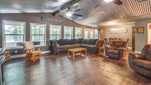 A spacious living room with a large sectional sofa, a wooden coffee table, and leather armchairs. The room has large windows allowing natural light and views of the outdoors. - Ferriday Lakehouse w/ Private Dock, Deck, & Yard! (Ferriday)