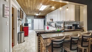 A modern kitchen with a wooden ceiling, a central island with bar stools, and stainless steel appliances. - Ferriday Lakehouse w/ Private Dock, Deck, & Yard! (Ferriday)