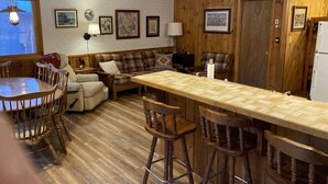 A cozy kitchen with wooden walls, a dining table with chairs, a bar stool area, and a refrigerator. - Charming and Cozy, 4-Season, Fence Lake Cottage with Beautiful Sunset View (Lac du Flambeau)