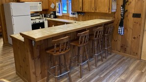 A kitchen with wooden cabinets, a central island with stools, a refrigerator, and a stove. - Charming and Cozy, 4-Season, Fence Lake Cottage with Beautiful Sunset View (Lac du Flambeau)