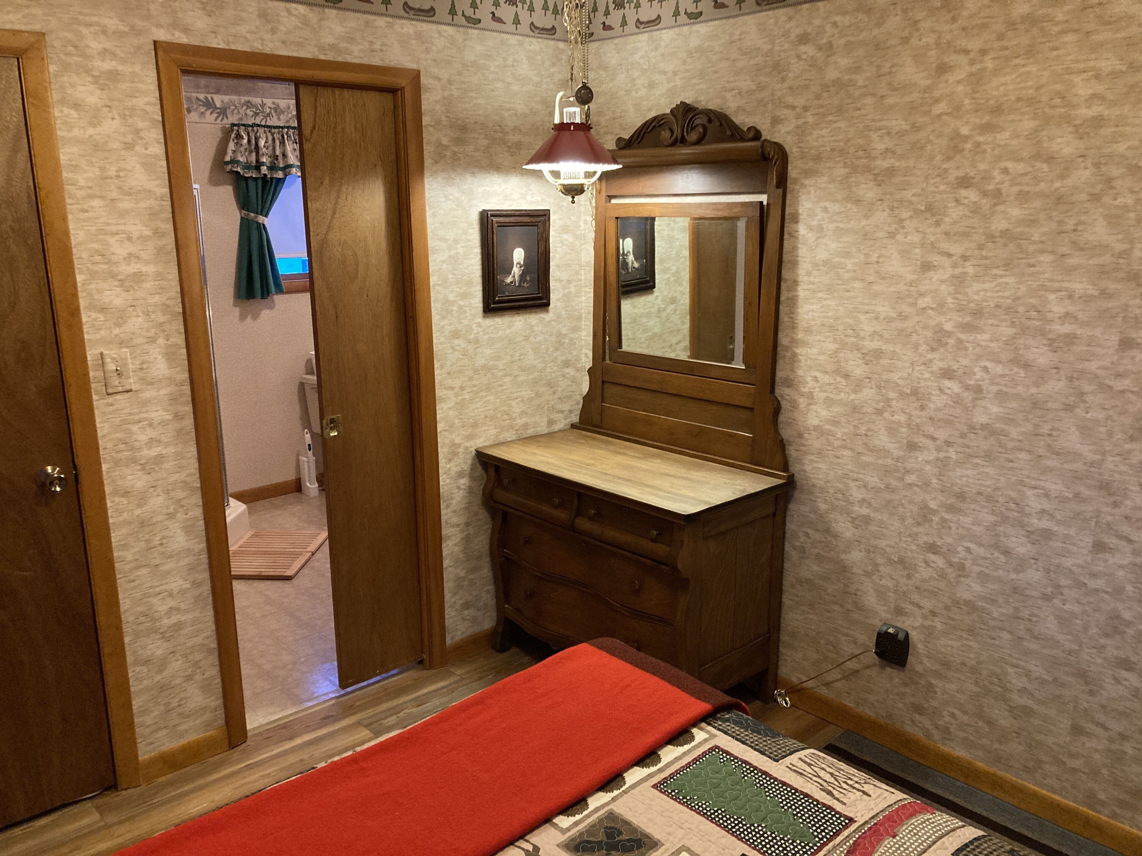 A bedroom with a wooden dresser, a mirror, a red rug, and a patterned rug on the floor.