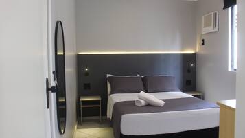 A modern hotel room with a large bed, bedside tables, a mirror, and a window with an air conditioning unit.