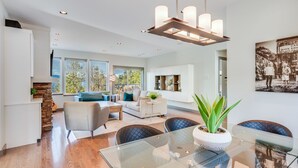 A modern living room with a glass dining table, comfortable seating, and a large window offering a view of the outdoors. - Bliss By the Bay (Brentwood Bay)