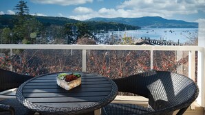 A balcony with wicker chairs and a table, overlooking a marina with boats and a mountainous landscape. - Bliss By the Bay (Brentwood Bay)