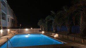 Ein Nacht-Schwimmbecken mit weißem Zaun und Palmen.