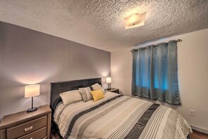A bedroom with a bed, nightstands, a lamp, and a window with curtains. - Ruidoso Cabin - Walk to Midtown Dining & Shops! (Ruidoso)