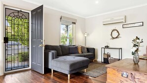 A living room with a grey sofa, a small table, a decorative wreath, and a nameplate on the wall.