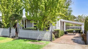 A residential property with a covered patio, a white picket fence, and a well-maintained lawn.