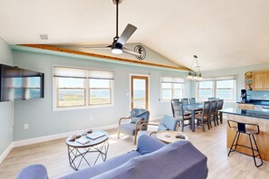 Relax in this spacious living area with a high ceiling, featuring a large flat-screen TV, dining area, and kitchen with a bar counter.