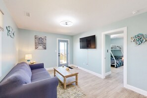 Cozy living space with a sofa, flat-screen TV, and door leading to a bedroom with a bed and bunk bed.