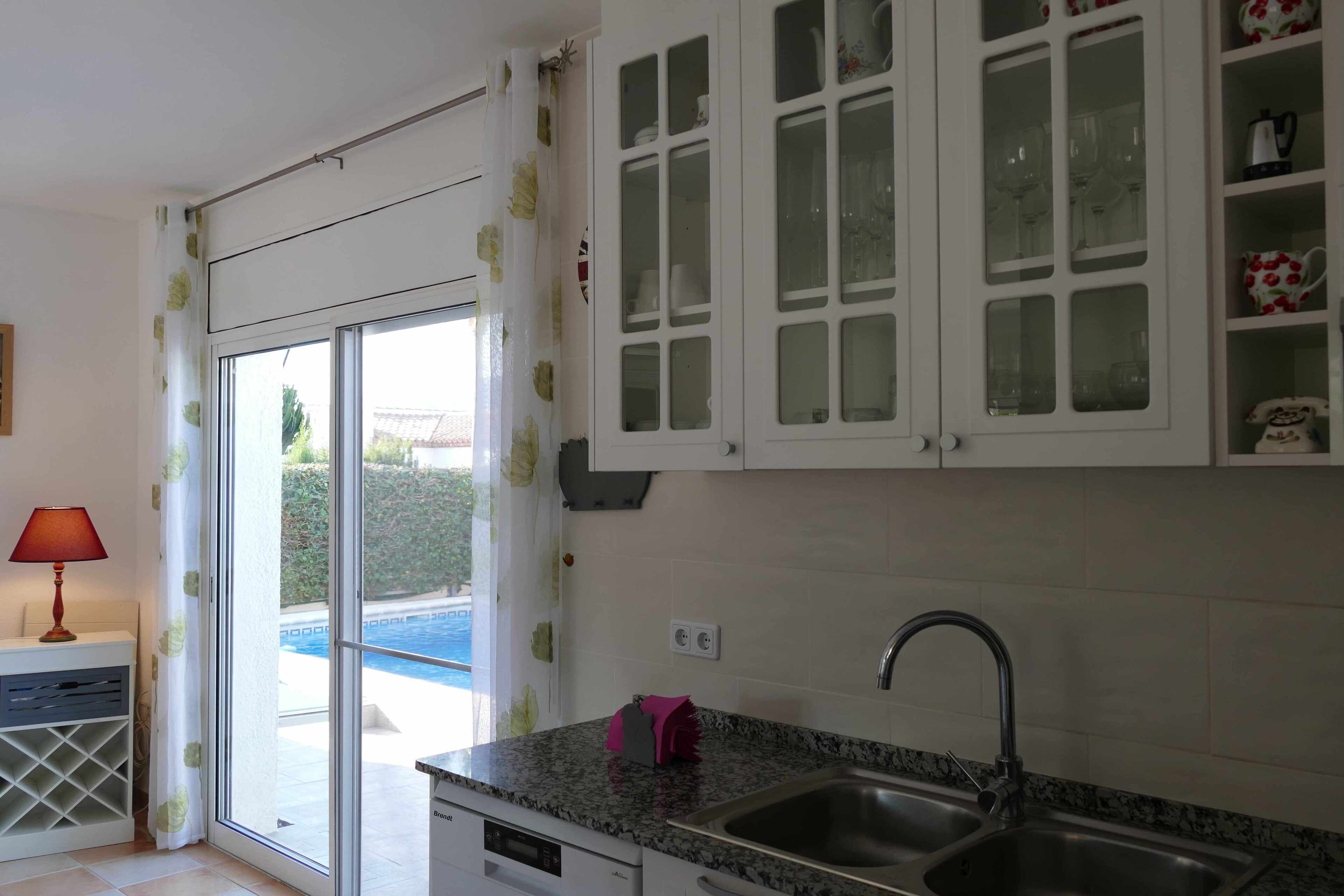 A kitchen with a granite countertop, stainless steel sink, and white cabinets with glass doors.