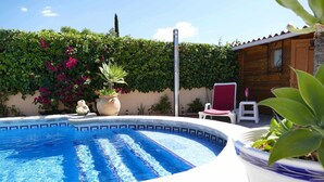 A swimming pool with a tiled edge, surrounded by greenery and a wooden fence.