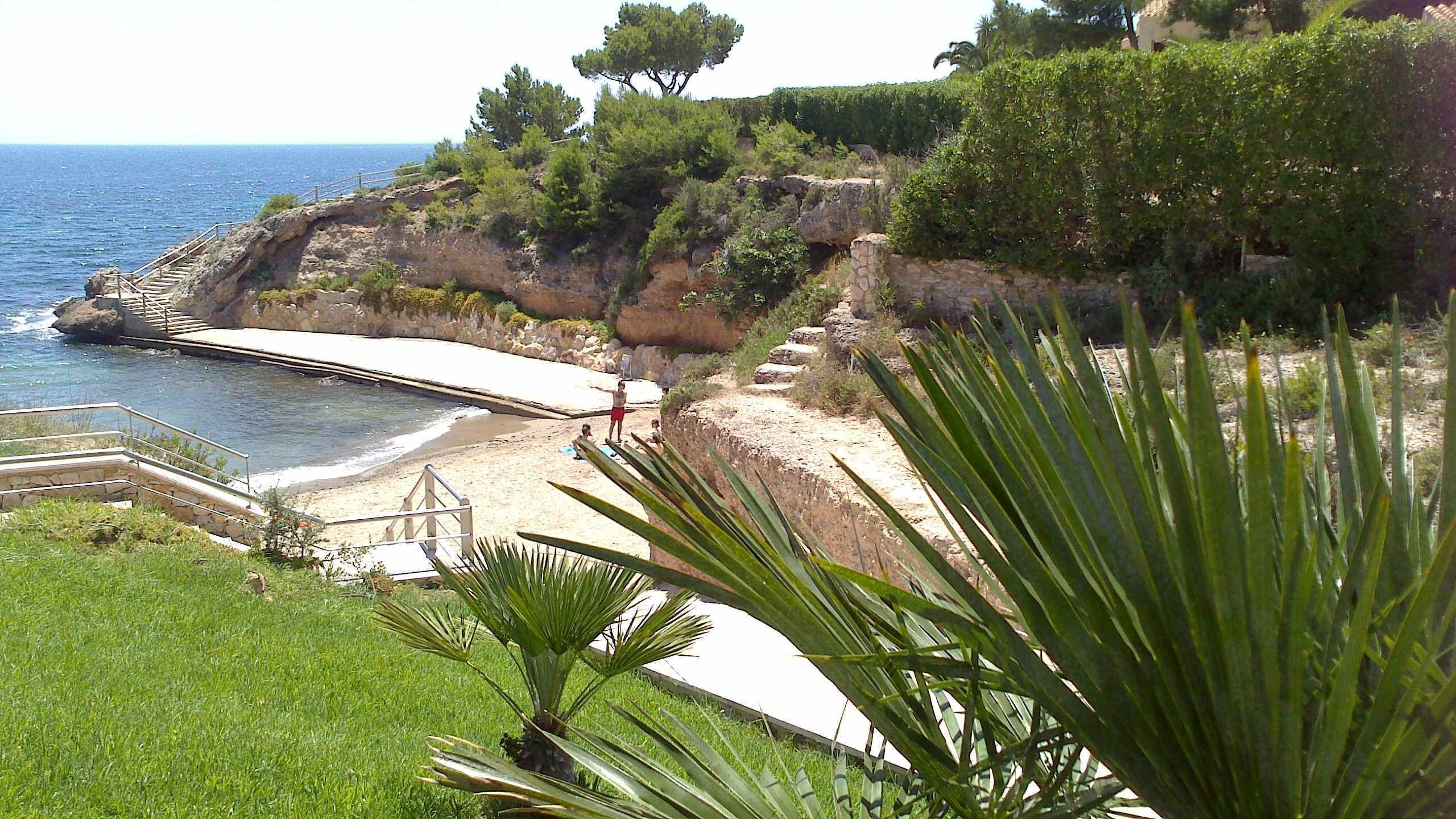 A coastal landscape with a beach, steps leading down to the water, and a rocky cliff.