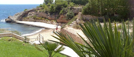 A coastal landscape with a beach, steps leading down to the water, and a rocky cliff.