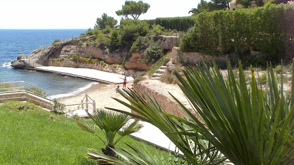 A coastal landscape with a beach, steps leading down to the water, and a rocky cliff.