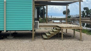 A small, single-story structure with a sloped roof, a covered outdoor area with a wooden deck, and a view of the ocean. - Waterfront & 4 minutes from the Gulf of Mexico (Perry)