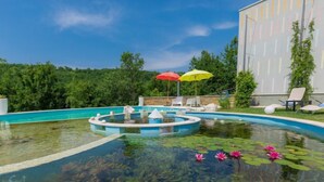 Una piscina con fuente, rodeada de sillones de descanso y sombrillas.