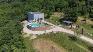 Una casa moderna con piscina, rodeada de exuberante vegetación y una colina con una torre al fondo.