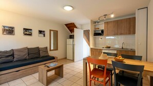 A compact living space with a sofa, coffee table, dining table with chairs, kitchenette, and a mirror.