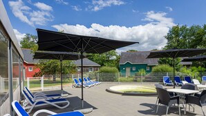 A poolside area with blue lounge chairs, umbrellas, and a table with chairs.