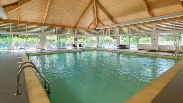 An indoor swimming pool with a wooden ceiling and tiled floor, surrounded by windows and lounge chairs. - Cosy apartment in villa for 6 people with pool, internet, TV, terrace and pets allowed (Marson)