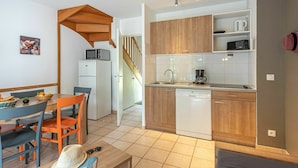 A compact kitchen with wooden cabinets, a dishwasher, and a microwave. There's a dining area with a table and chairs, and a staircase leading to another level. - Cosy apartment in villa for 6 people with pool, internet, TV, terrace and pets allowed (Marson)