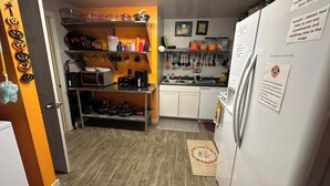 Eine kleine Küche mit Mikrowelle, Toaster und Spüle. Verschiedene Küchenutensilien hängen an der Wand und es steht ein Kühlschrank mit einem Brandschutzhinweis darin.