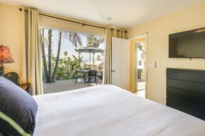 Ein Hotelzimmer mit Bett, Fernseher, Tisch mit Stühlen und Blick auf Palmen sowie ein Gebäude.