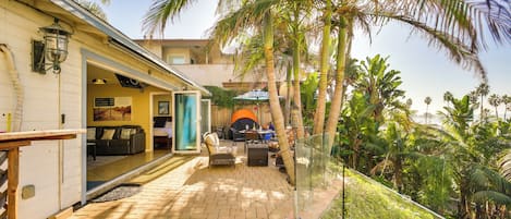 A patio area with a brick floor, outdoor furniture, and a view of palm trees.