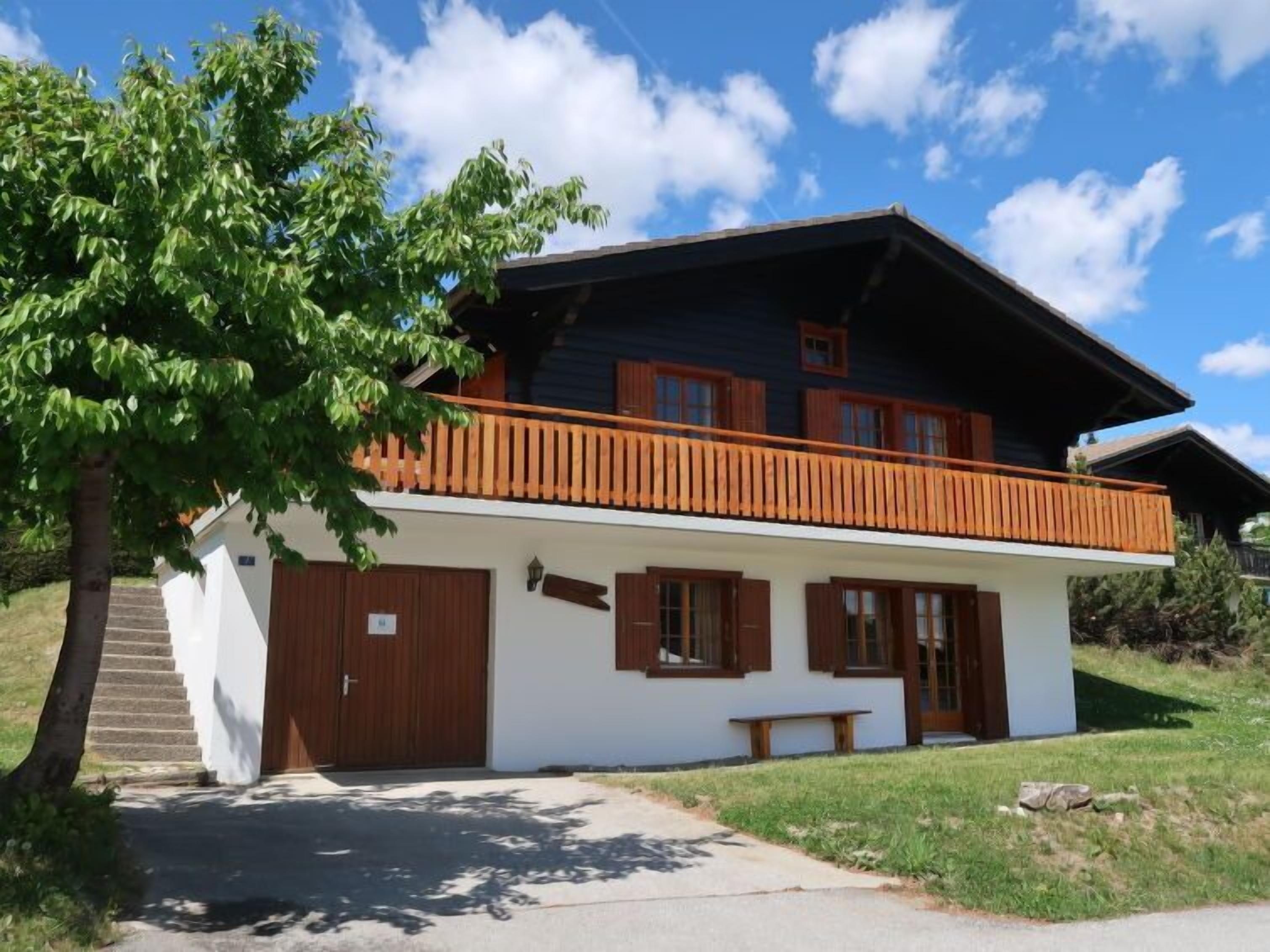 A two-story chalet with a wooden balcony, a covered porch, and a stone staircase leading to the entrance.