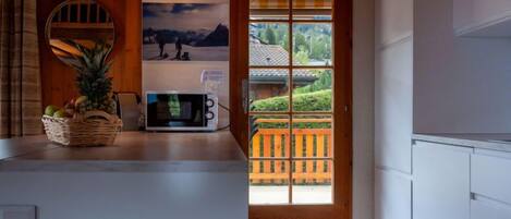 A kitchen with a microwave, a fruit basket, and a view of a wooden deck and greenery outside.