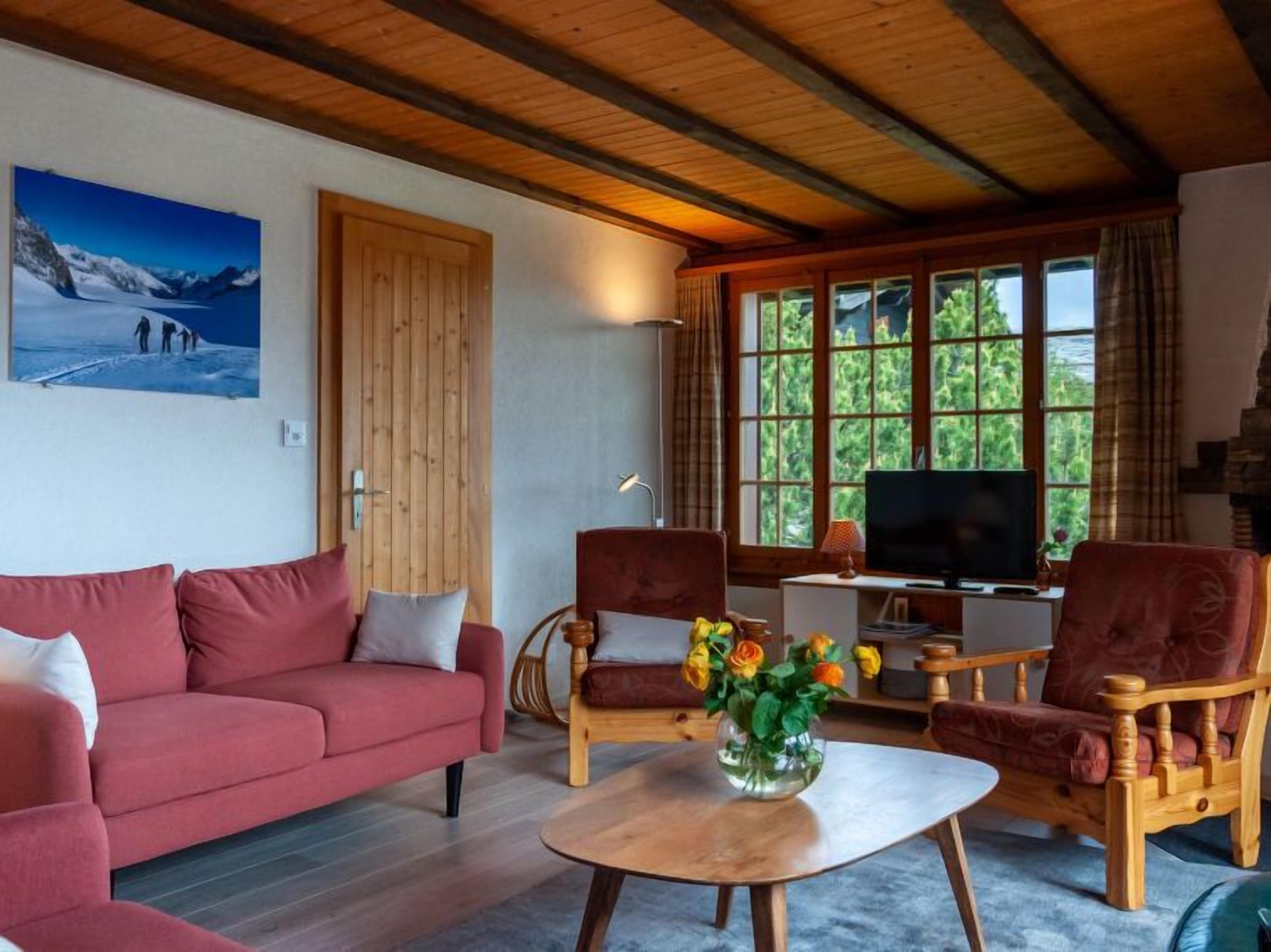 Un salon chaleureux avec un canapé rouge, des chaises en bois, une table basse et un téléviseur.
