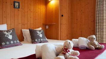 Ein gemütliches Zimmer mit Holzwänden, einem Bett mit weißer Bettwäsche, zwei Kopfkissen mit Hirschmotiven und zwei Teddybären auf dem Bett.
