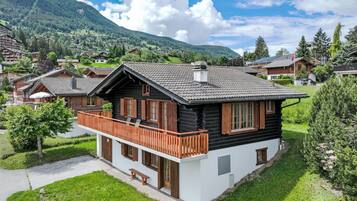 Ein Chalet mit Balkon, umgeben von üppigem Grün und einer Bergkulisse.
