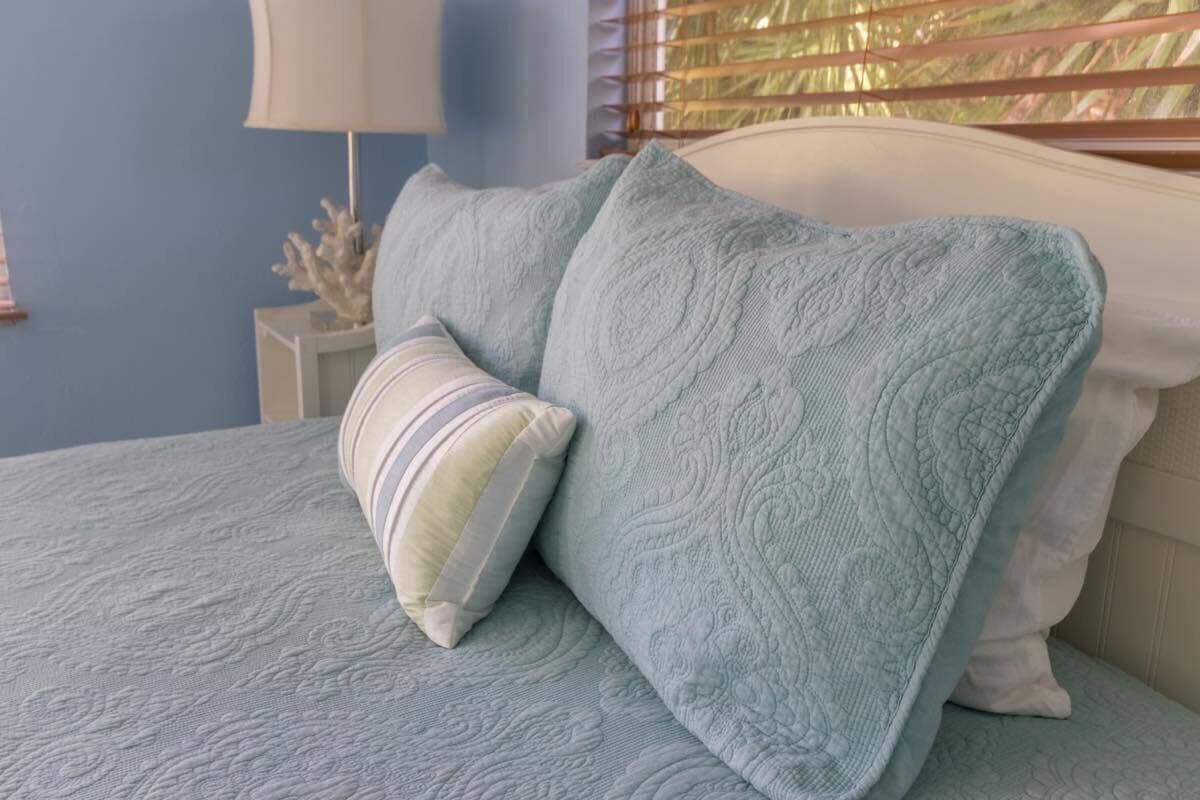 A bed with a light blue quilt and two pillows, one striped and one solid.