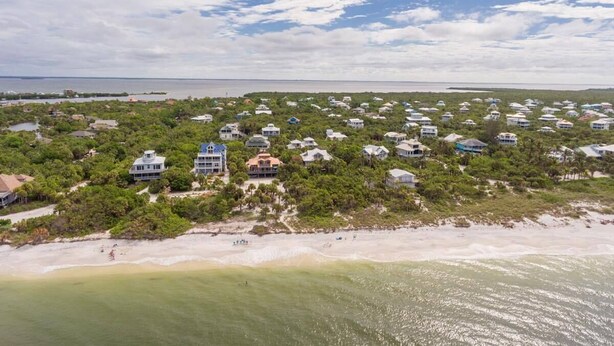 Vue aérienne d’un quartier résidentiel situé sur la côte, avec des maisons entourées d’une végétation luxuriante et une plage.